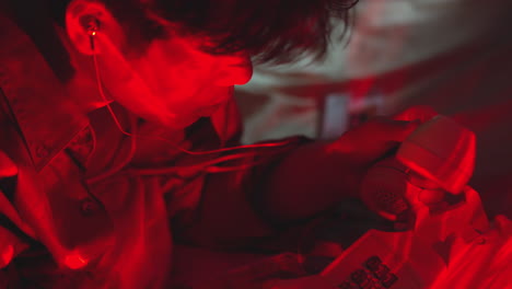 young asiatic male in red light room trying to make a phone call using an old vintage receiver