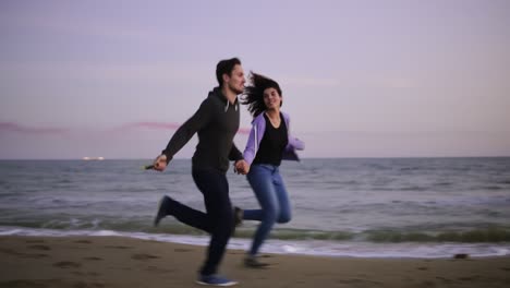 young happy couple running with colored smoke grenade in their hands by the sea during sunset. fun, colorful smoke around them