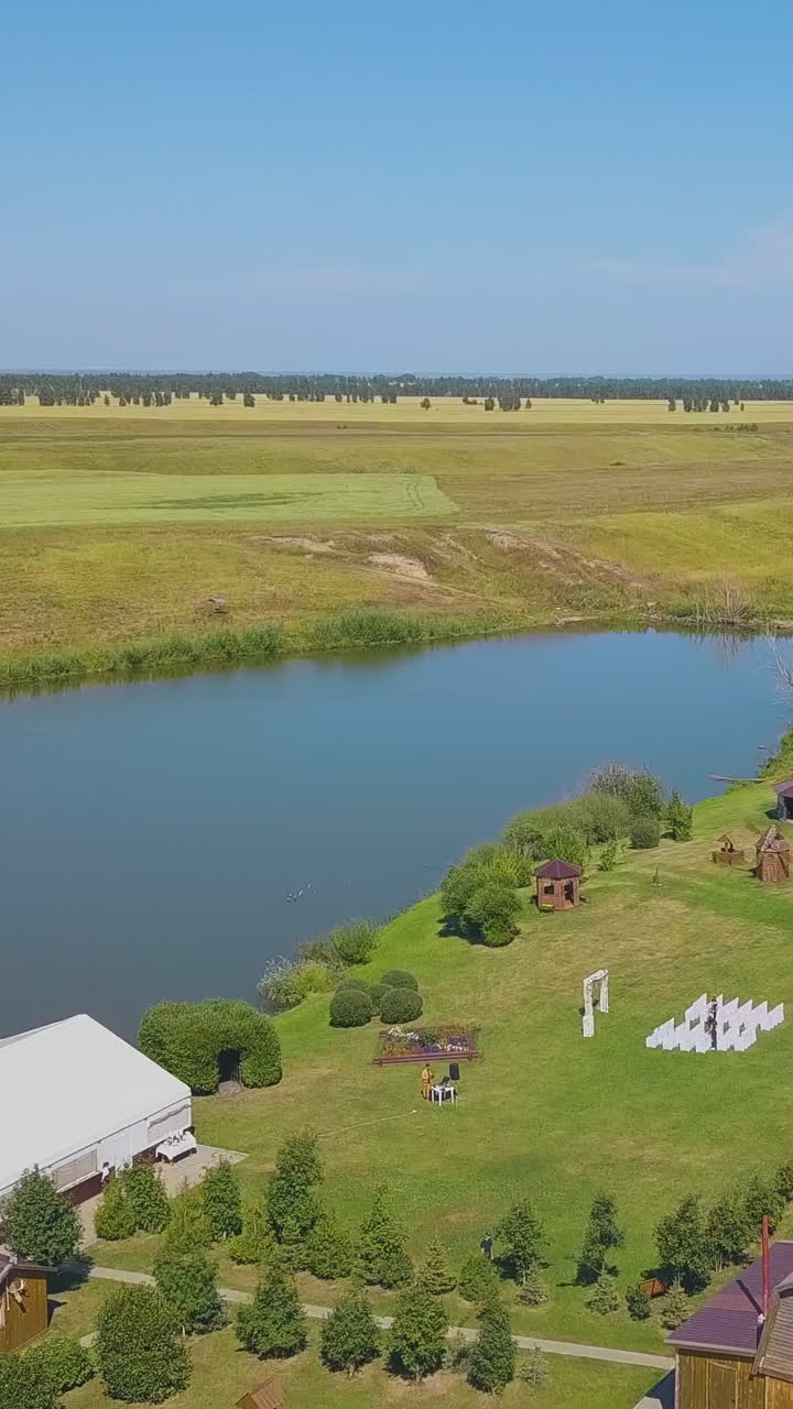 white wedding venue with arch and seats on green meadow at calm lake under blue sky on nice autumn day upper view