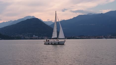 Touristen-Genießen-Eine-Entspannte-Segelbootfahrt-Auf-Dem-Lago-Maggiore,-Während-Die-Sonne-Hinter-Der-Alpenkette-Untergeht