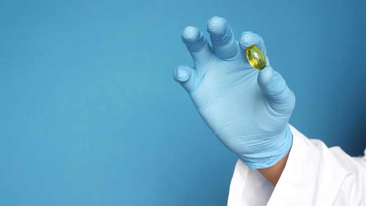 mano con guantes azules sosteniendo una cápsula amarilla