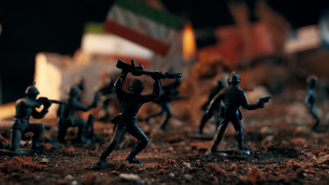 Miniature diorama depicting a battlefield with plastic toy soldiers. Usa and iranian flags are visible in the background among the ruins