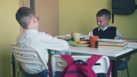 escolares felices hablando sentados en la mesa con el almuerzo y los libros