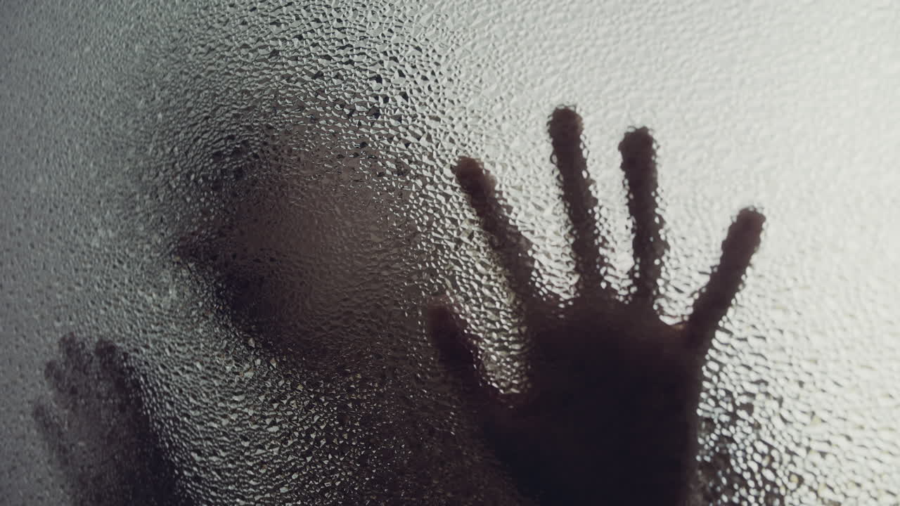 A female silhouette behind the frosted window touches the glass slowly