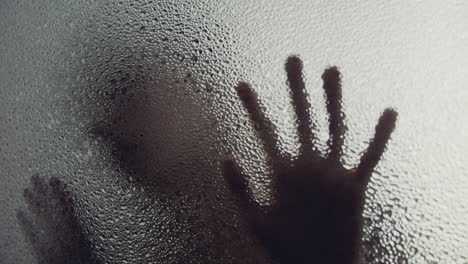 a female silhouette behind the frosted window touches the glass slowly