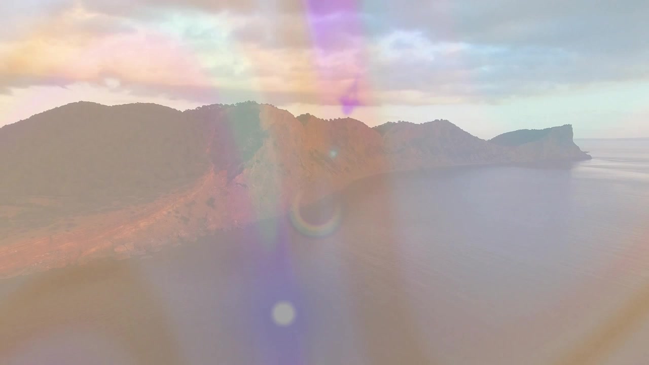 Inquadratura iniziale che genera raggi arcobaleno che si muovono su una cresta costiera rocciosa, rivelando le ombre del tramonto.