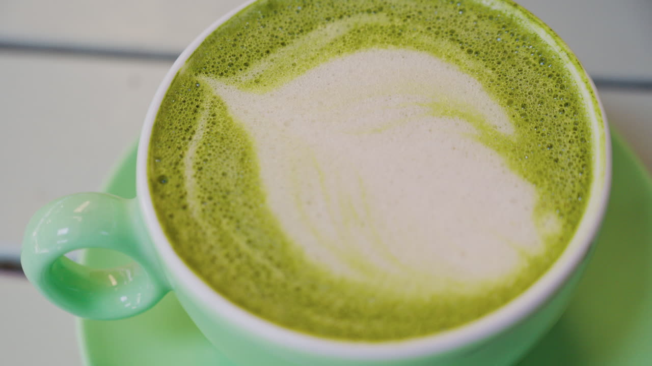 Close up of a matcha latte in a green cup on a terrace table
