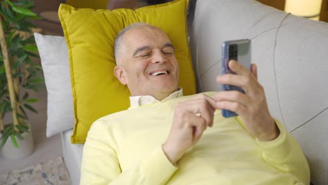 Happy-old-man-lying-on-sofa-using-phone.