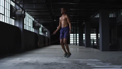 shirtless african american man skipping the rope in an empty urban building