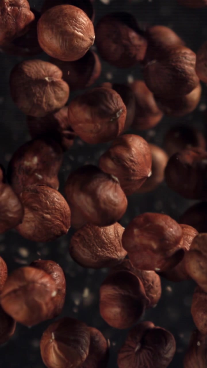 Nocciole crude che galleggiano al rallentatore su sfondo scuro