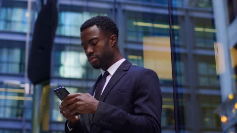 Young-Businessman-Wearing-Suit-Taking-Call-On-Mobile-Phone-Standing-Outside-Offices-In-The-Financial-District-Of-The-City-Of-London-UK-Shot-In-Real-Time