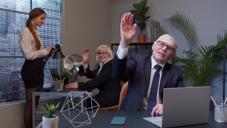 senior businessman with colleagues team waves palm in hello gesture welcomes someone in office