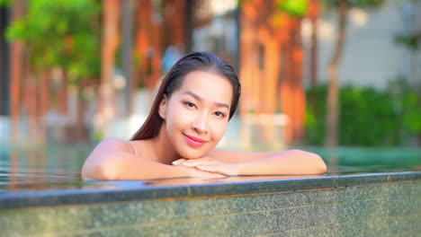 close-up of a pretty young woman leaning along the edge of an infinity pool as water drips over the edge