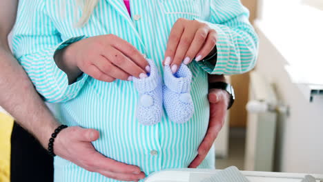 loving couple expecting a baby. future mom steps little sock by her big belly. male hands stroke the abdomen. close up.