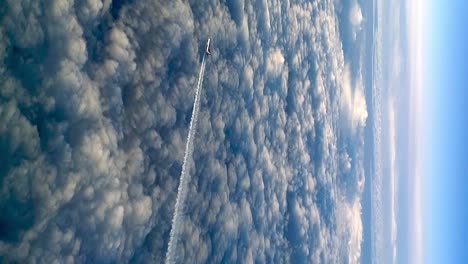 Unusual-view-from-cockpit-of-flying-airplane-above-clouds-leaving-long-white-condensation-vapor-air-trail-in-blue-sky,-zoom-out-VERTICAL-format