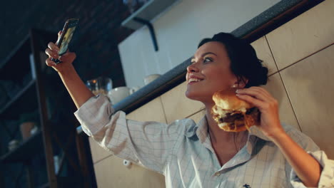 hungry girl eating burger on floor. woman making selfie photo with burger.
