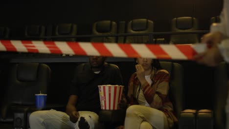 african american young couple came to the movie theatre watching film while a man in a protection costume stretching warning