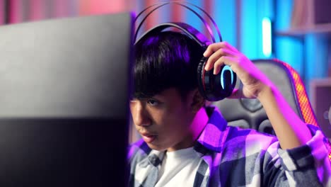 close up of asian teen boy gamer wearing head phones and start play video game on computer