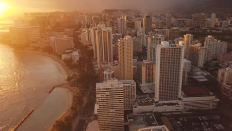 panning aerial drone slowly flying over a colorful honolulu skyline while sunset in oahu, hawaii with waikiki beach as a special point of interest.