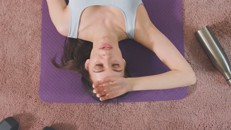 overhead shot of woman resting on exercise mat at home after workout - shot in slow motion