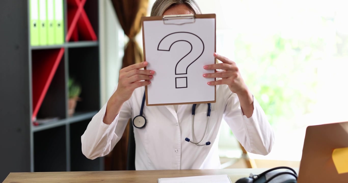 Un medico appare perplesso mentre mostra un cartello con un punto interrogativo, evidenziando la sua confusione