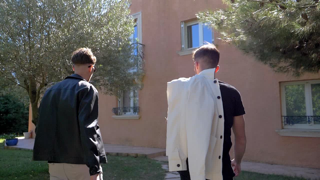 slow motion shot of men walking with a jacket over their shoulder to a house