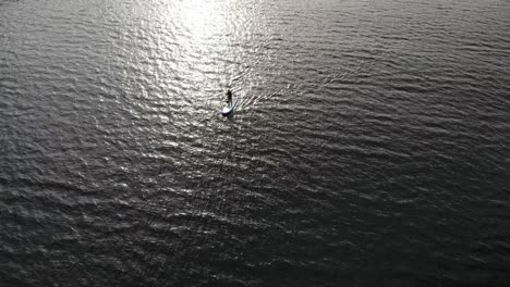 Drone-footage-of-a-backlit-person-on-stand-up-paddle-board-on-water