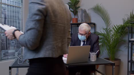 Elderly-man-boss-with-woman-secretary-in-medical-mask-working-in-office-during-coronavirus-pandemic