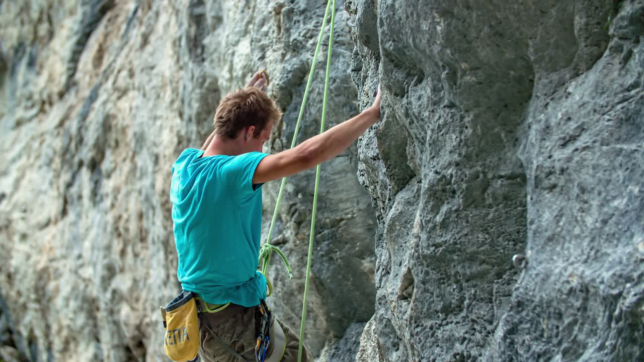 Young athletic man practicing rock climbing on a steep high wall with ropes and other equipment