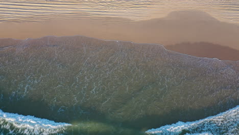 Aerial-view-overlooking-waves-hitting-the-Fraser-island-beach,-in-sunny-Australia