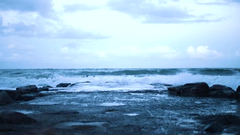 crabs eye view of small, cold waves crashing against a rocky jetti that stretches into the sea as the setting sun leaves a blue tint in the sky, water and clouds