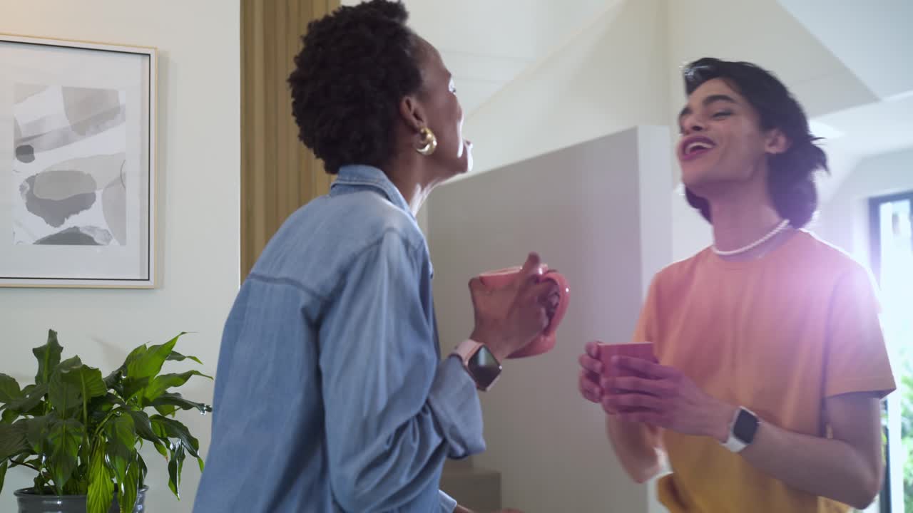 Amigos diversos parados perto da escadaria, inalando o aroma de café e rindo enquanto bebem de canecas rosas.