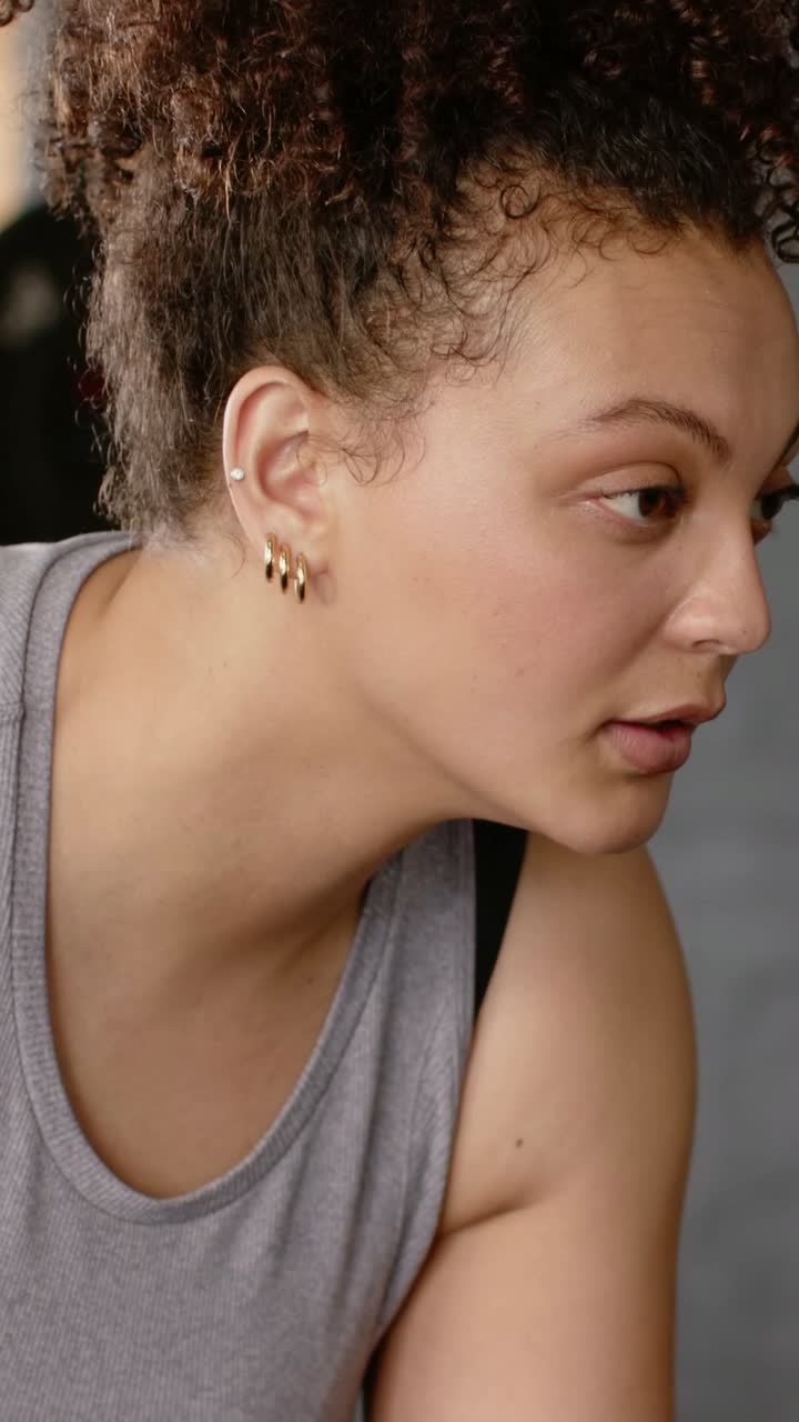 Video verticale: Donna che respira e si allena, con canotta grigia, che si abbassa in posizione plank in palestra; bilanciere, anelli.