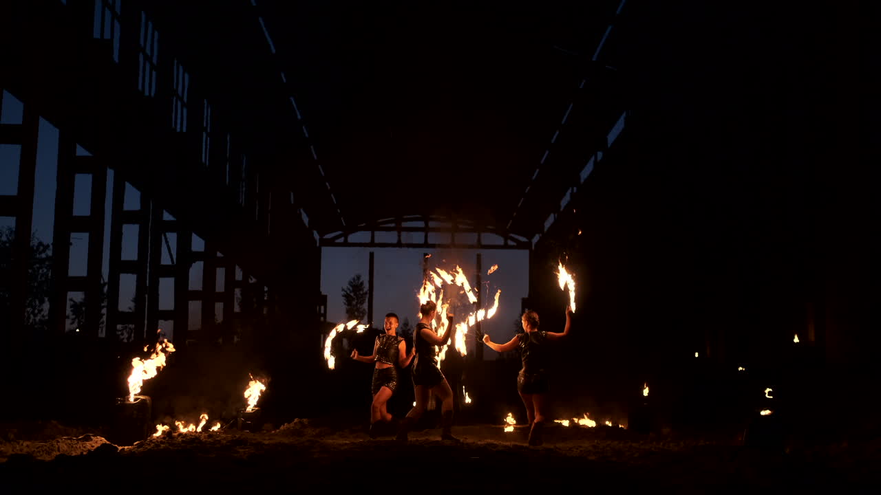 A group of people with fire and torches dancing at sunset in the hangar in slow motion. Fire show.