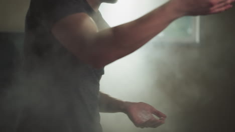 man claps hands spreading talc powder cloud in gym closeup. boxer uses talcum product for palms in martial arts club slow motion. sports supplies