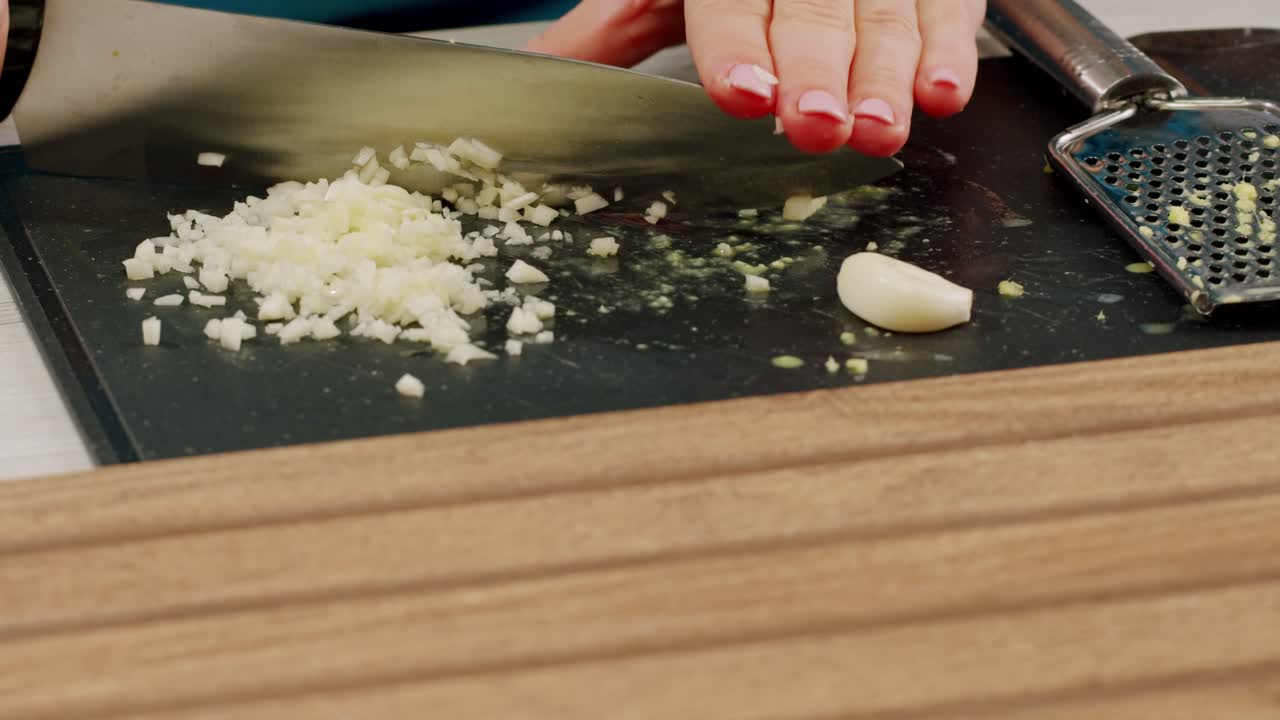 Woman chopping garlic on wooden cutting board at domestic kitchen. High quality 4k footage