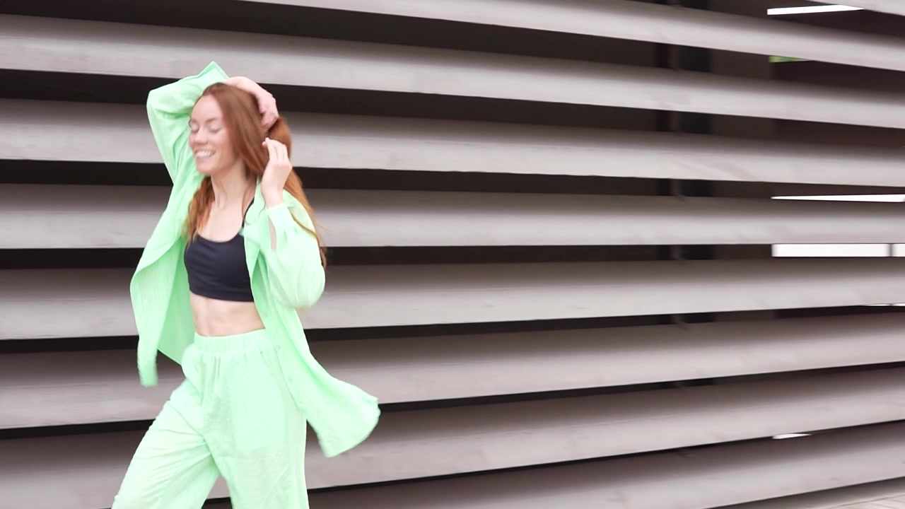Donna che balla con un elegante outfit verde neon su uno sfondo architettonico moderno.