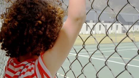 Rear-view-of-mixed-race-schoolgirl-standing-near-wire-mesh-fence-at-school-4k