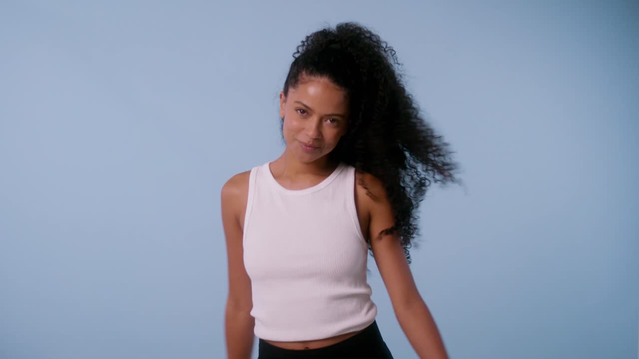 Black woman with curly hair smiles and spins with arms open in fun beauty shoot