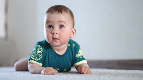 happy smiling infant boy lies on belly on the floor. active baby claps his hands and feet over the carpet. light backdrop.
