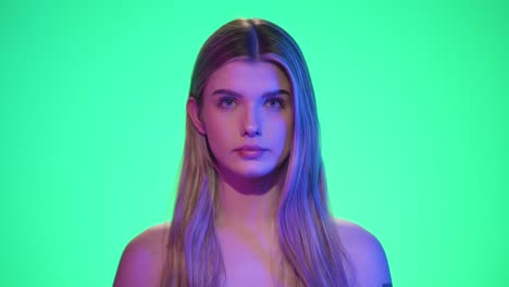 static shot of a young pretty woman making gestures with her hand to symbolize that something has passed in front of green background with blue and purple contrast in her face in slow motion