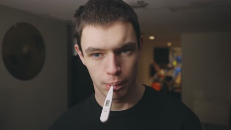 young man checking his body temperature using an oral digital thermometer - health care concept - closeup shot