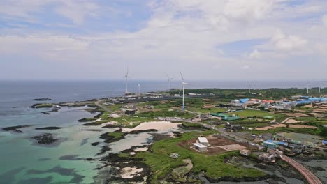 Stunning-drone-view-of-Woljeong-Beach's-pristine-shores,-a-tranquil-oasis-on-beautiful-Jeju-Island,-with-a-unique-view-of-Wind-Turbines-in-right-on-the-waters-edge