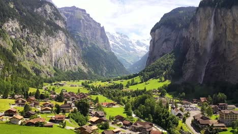 Impresionante-Vista-Aérea:-Tranquilo-Pueblo-Del-Valle-De-Lauterbrunnen-En-Un-Día-Soleado-De-Verano,-Entre-Montañas-De-Los-Alpes-Suizos,-Prados-Verdes-Y-Frescos-Y-La-Cascada-Staubbach