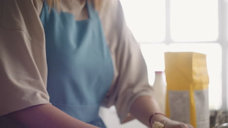 Una-Mujer-Adulta-Con-Delantal-Azul-Está-Amasando-Masa-Con-Las-Manos,-Vista-De-Cerca-En-La-Mesa,-Ama-De-Casa-Está-Cocinando-Para-La-Familia