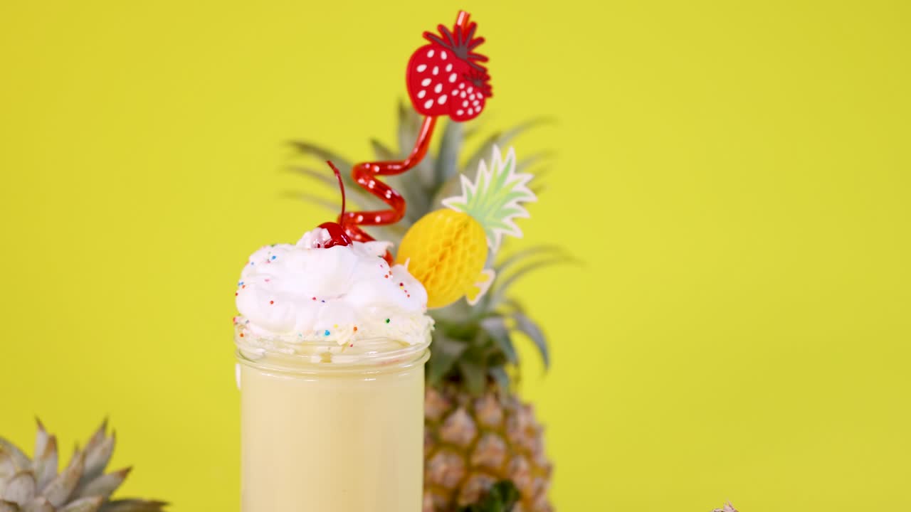Pineapple smoothie in glass with whipped cream, fruit garnish, bright lighting, static camera, vibrant background