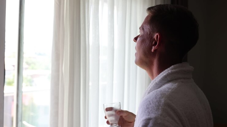 Man drinking from a glass by the window