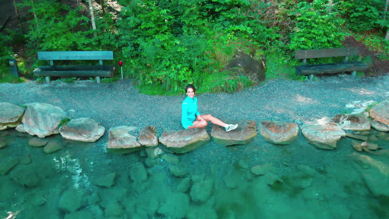 Ripresa drone di una donna anziana sportiva seduta in riva a un bellissimo lago immersa nella natura