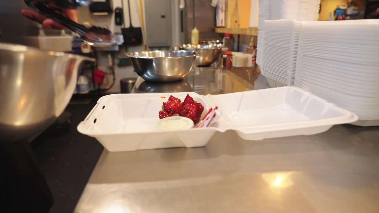 Filmato in 4K ravvicinato di alette di pollo piccanti alla Louisiana servite su un piatto da asporto in Texas, fresche dalla ciotola di marinatura, che cattura la salsa piccante, la consistenza croccante e la presentazione del cibo caldo.