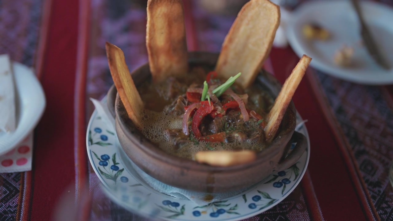 Traditionell lamagryta serverad i en lerkruka med krispiga potatisklyftor, fyllig buljong och regionala ingredienser rotade i andinska kulinariska traditioner, avslöjande bild i slow motion